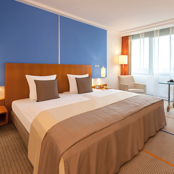 Das Bild zeigt ein modern eingerichtetes Hotelzimmer mit einem großen Doppelbett im Mittelpunkt.